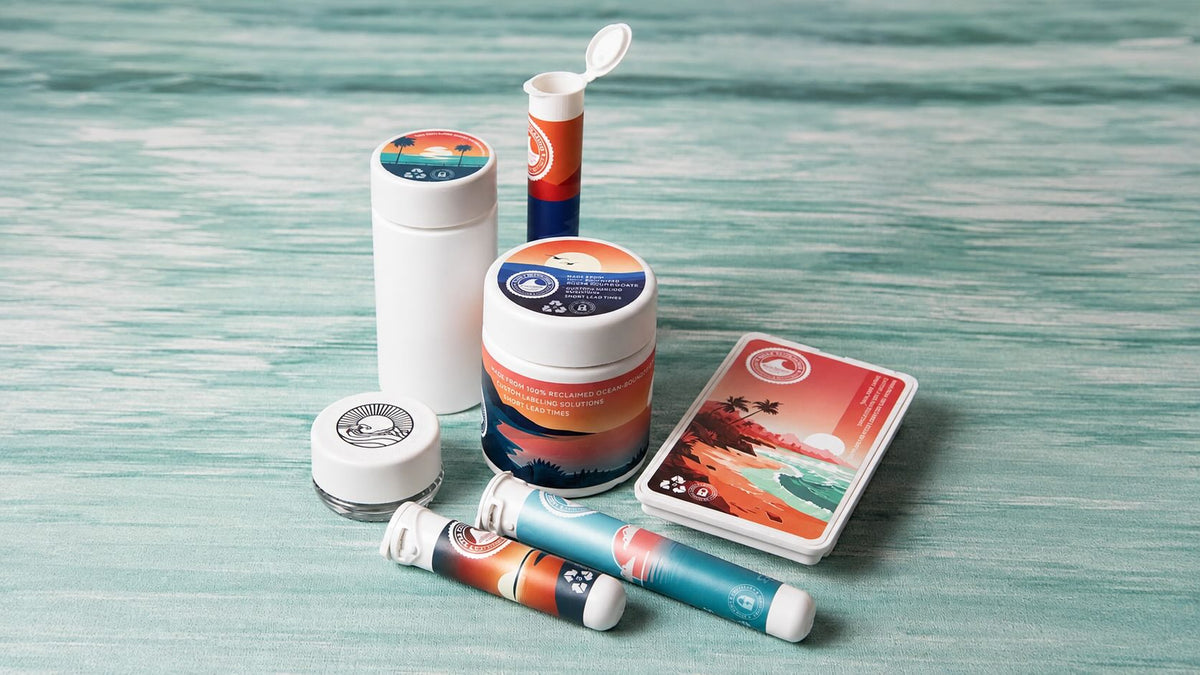 Assortment of reclaimed ocean-bound plastic cannabis packaging, including jars, pre-roll tubes, and a multipack, on a teal wood background.