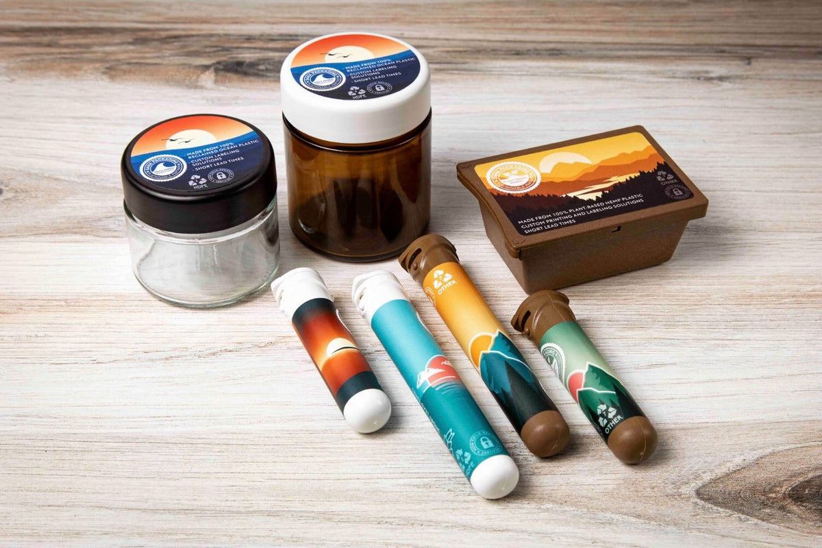 Glass jars with reclaimed ocean-bound plastic lids, a plant-based hemp plastic container, and custom pre-roll tubes arranged on a light wood surface.