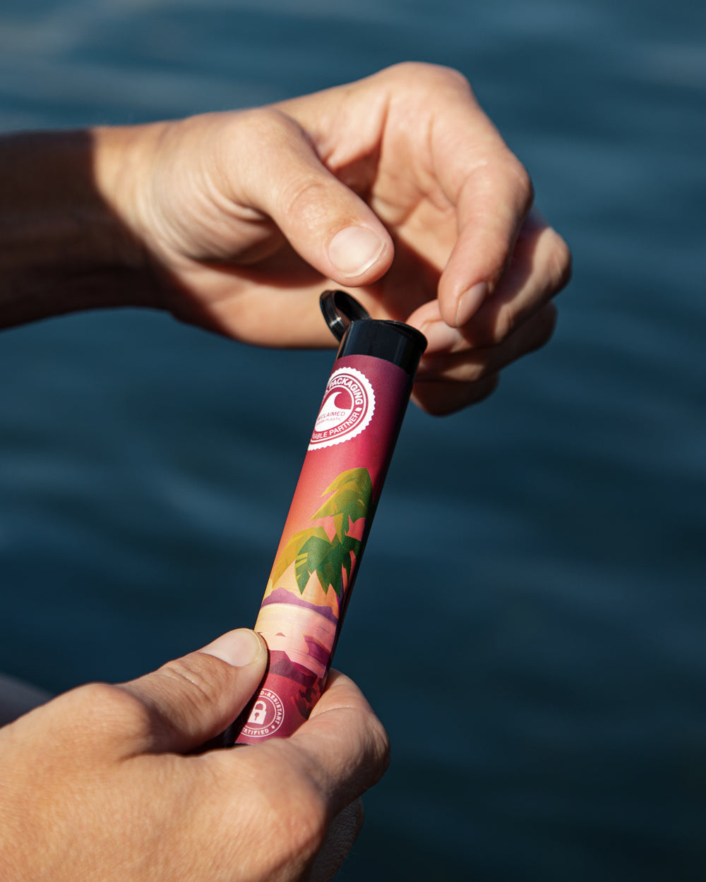 Hands opening a custom-labeled black 116mm Pop-Top Ocean Tube outdoors