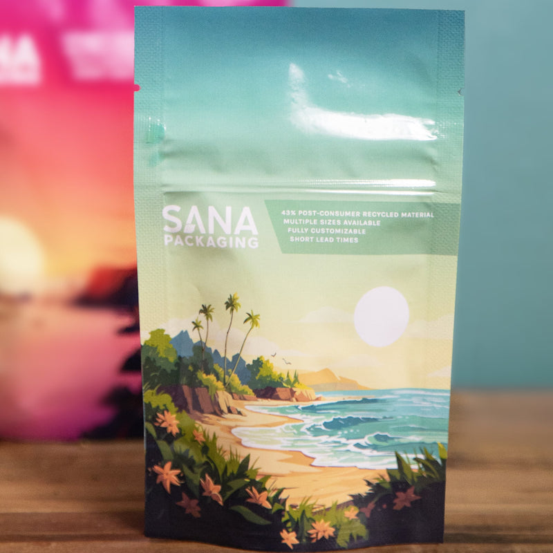 Teal Sana Packaging pouch printed with a beach scene, in front of a blurred sunset pouch